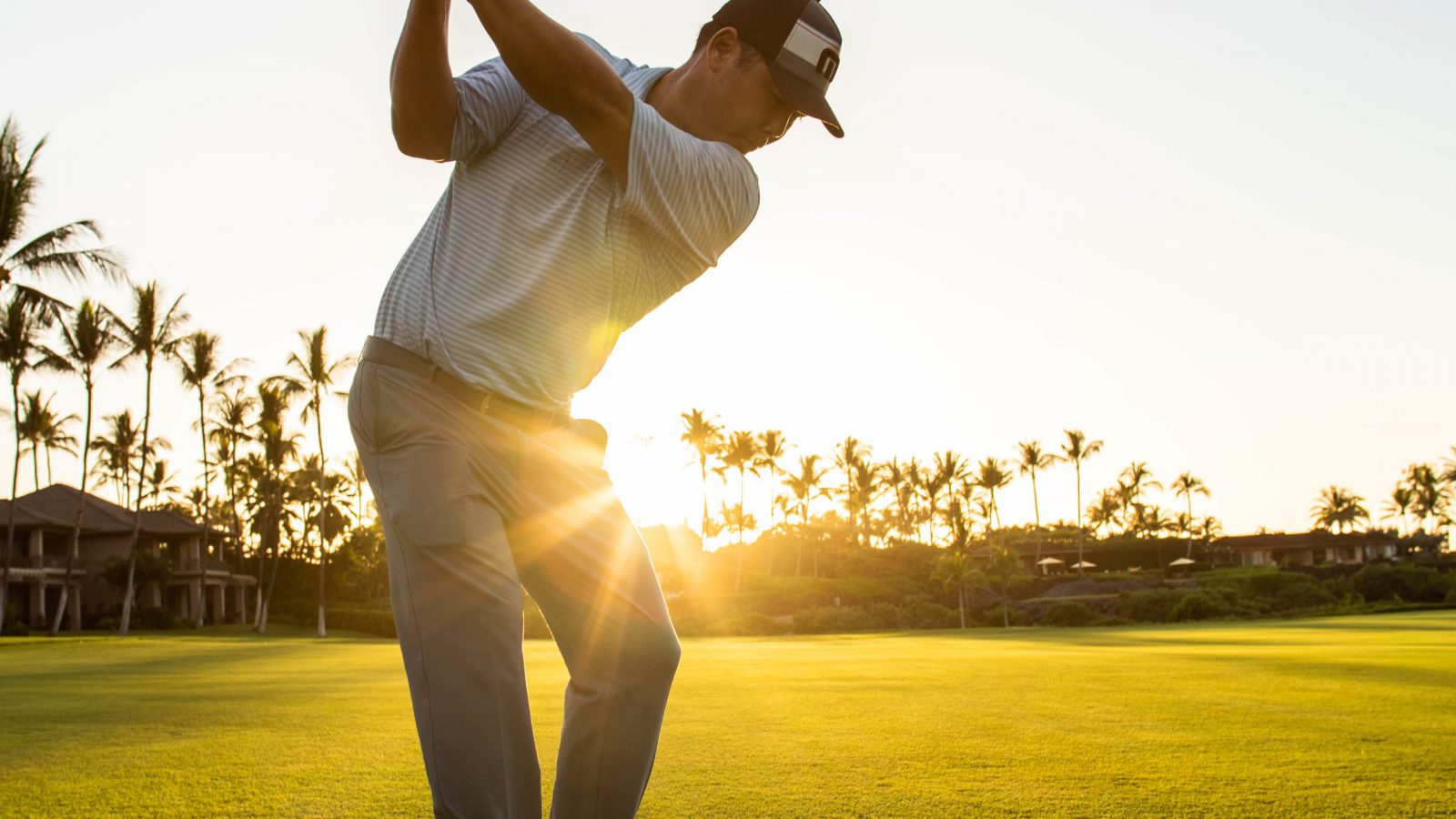 Golf Pro Garratt Okamura takes a swing a golf ball with setting sun in background